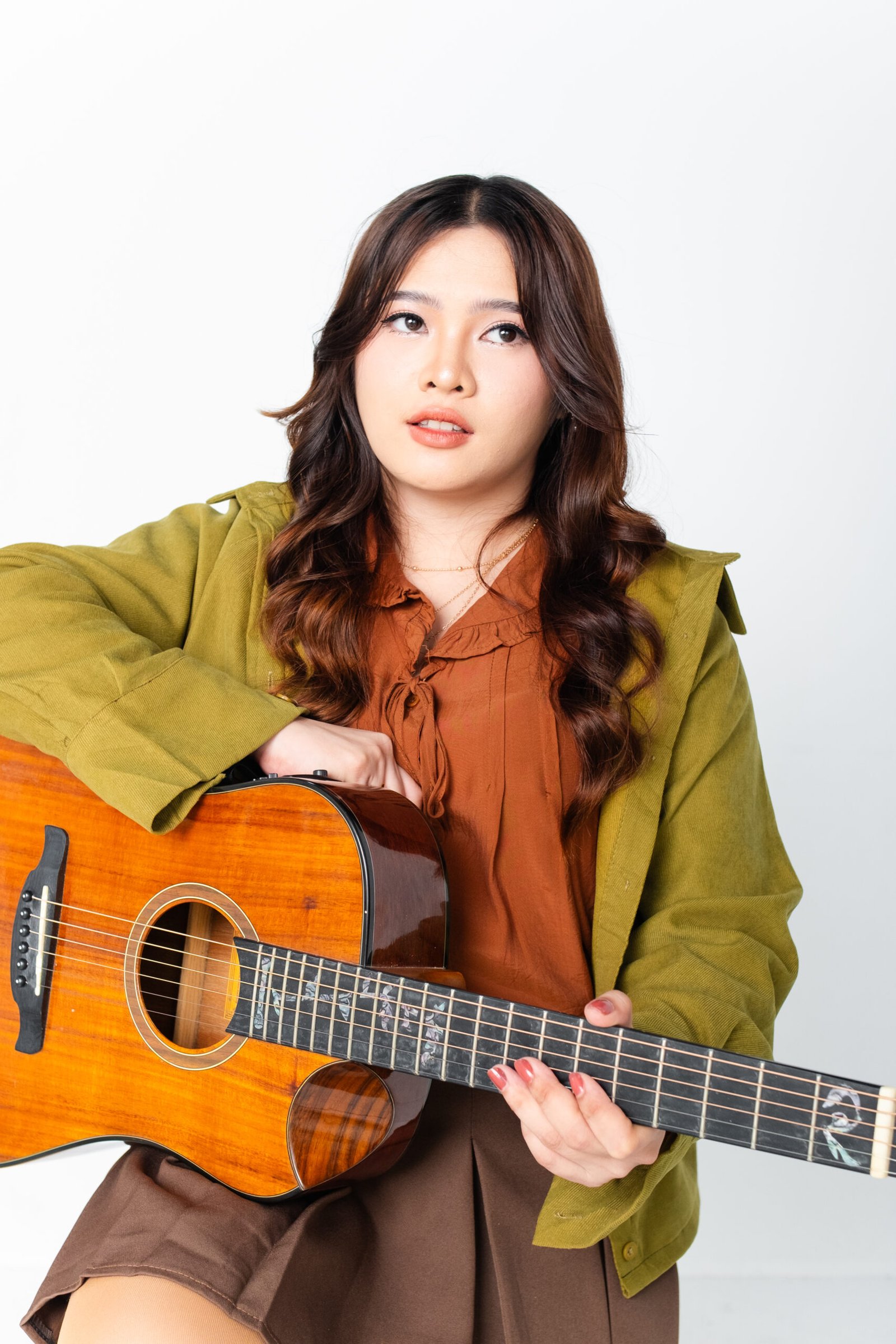 Kyla Jean in a studio portrait, resting on her acoustic guitar